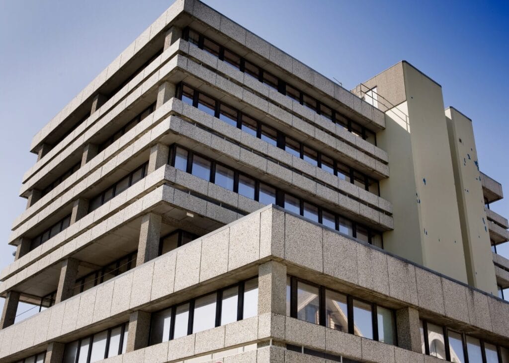 Modern concrete office building with multiple stories and large windows.